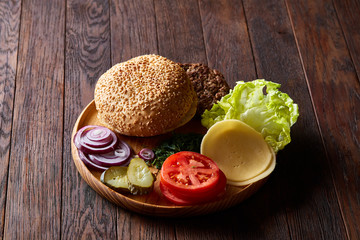 Yummy hamburger ingredients artistically organized on wooden plate, close-up, top view, selective focus