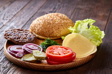 Yummy hamburger ingredients artistically organized on wooden plate, close-up, top view, selective focus