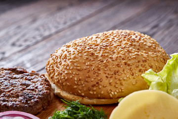Yummy hamburger ingredients artistically organized on wooden plate, close-up, top view, selective focus