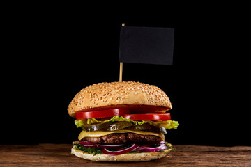 Classic American cheeseburger with black flag on the top over dark background, close-up, selective focus