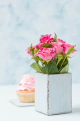 Obraz na płótnie Canvas Bouquet of roses in retro shabby chic vase and cupcake with pink cream decoration.