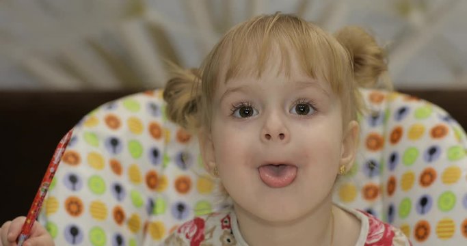 Beautiful two years old girl shows her tongue. Cute blonde child. Brown eyes. Close up