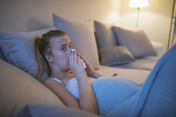 Sick young woman under blanket in domestic interior