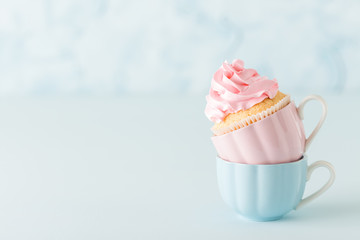 Cupcake with pink buttercream decoration in two cups on blue pastel background.