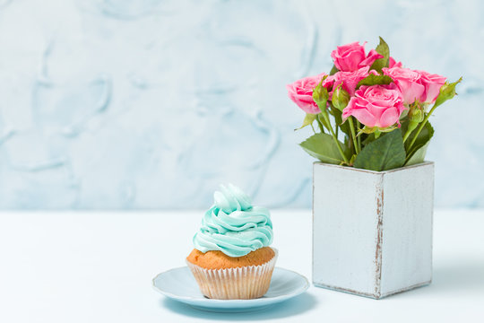 Blue pastel horizontal banner with cupcake with blue decoration and bouquet of pink roses in retro shabby chic vase.