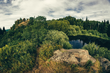 Obraz premium Lake on top of hill, surrounded by rocks and thickets, captured by the fisheye lens.