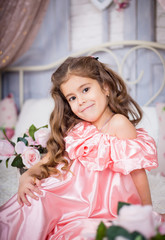 Obraz na płótnie Canvas cute girl with beautiful curly hair in a pink dress posing on a delicate floral provence background
