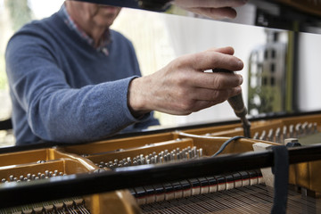 closeup of hand and tools of tuner working on grand piano