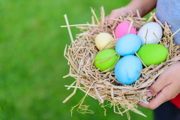 Fototapeta na wymiar A kid holding Colorful of Easter eggs in nest on grass green background.