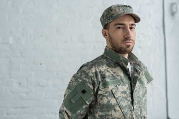 portrait of soldier in military uniform looking at camera against white brick wall