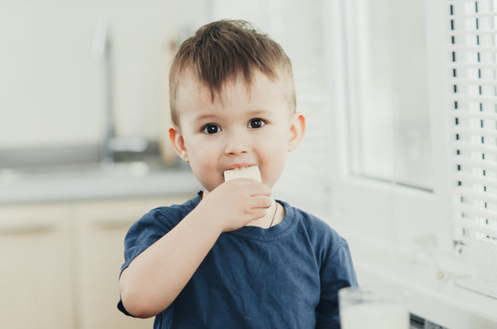a little charming boy eats waffles in the kitchen and drinks milk