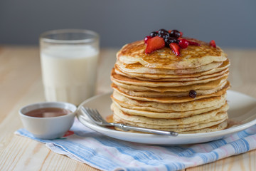 Pancakes with berries and maple syrup on a light table. Pancakes and milk.