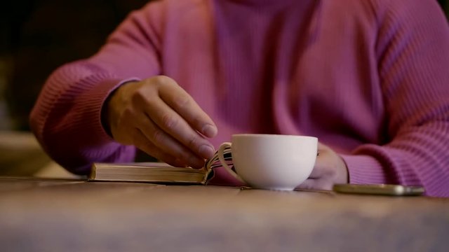 A man in a cafe drinking coffee and reading a book. Slow motion