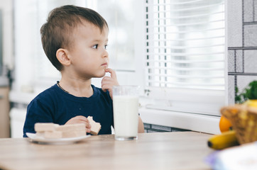 a little charming boy eats waffles in the kitchen and drinks milk