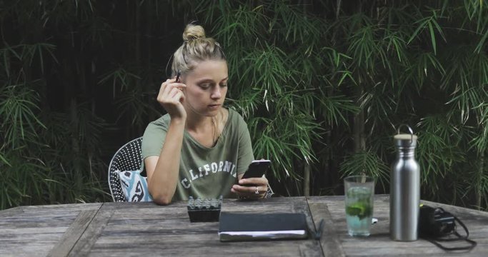 young pretty rexaxed girl or woman having rest on nature, smoking rollup (sigarette), chilling, checking her phone, searching in internet, listening music