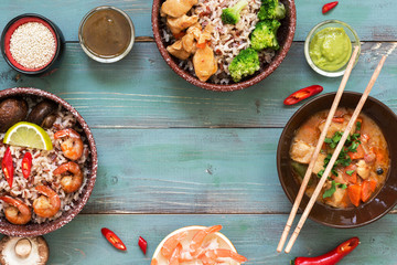 Shrimp with rice, sauces, chicken and mushrooms on a blue wooden background. A frame from Asian dishes. Top view, copy space.