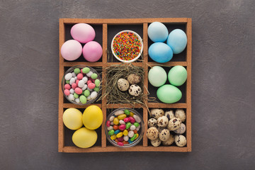 Colored easter eggs and small candies in frame on gray background