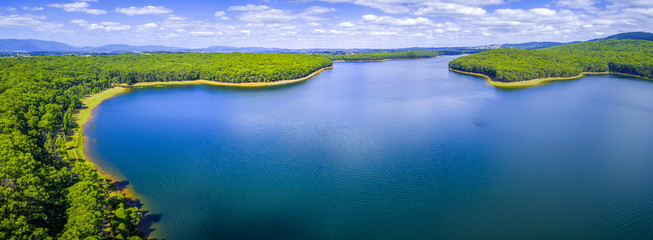 Aerial panorama of beautiful blue lake and forest under white fluffy clouds in Australia