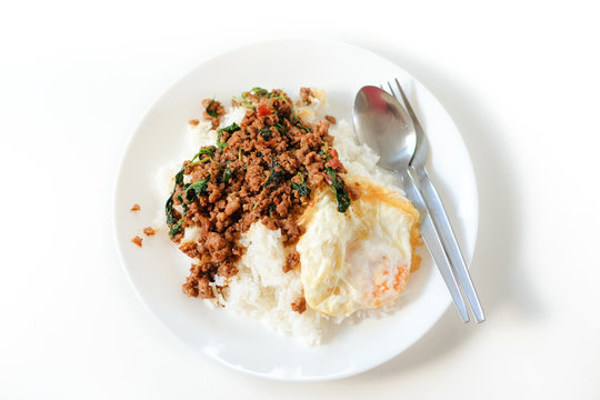 Rice topped with stir-fried pork and basil serve with fried egg on white plate & spoon, fork set on the table - Thailand food popular & nice to eat concept.