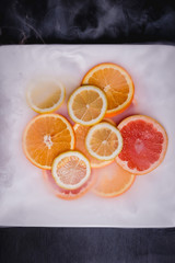 Different citrus fruits slices served on a white plate with fork and knife on black background.