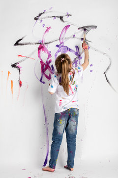 Little girl decorating a white wall with paint