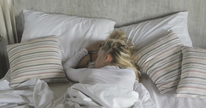 young pretty girl or woman sleeping on white bed, covered by blanket, lots of pillows