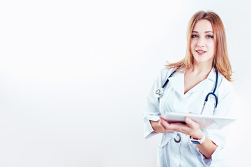 doctor in white medical coat  is using a tablet and smiling while standing against window