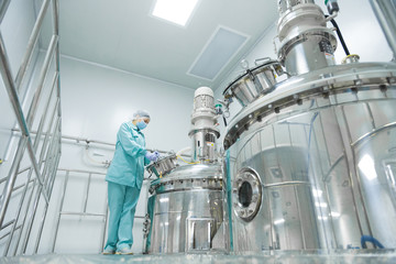 Pharmaceutical factory woman worker in protective clothing operating production line in sterile...