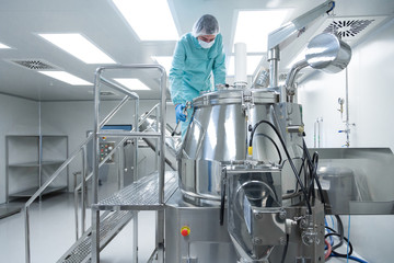 Pharmaceutical factory man worker in protective clothing operate production line in sterile working...