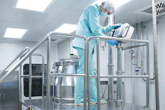 Pharmaceutical factory man worker in protective clothing operate production line in sterile working conditions