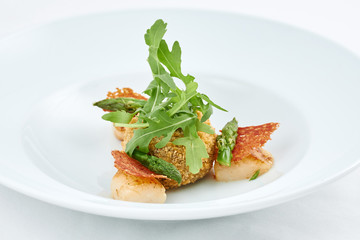 Delicious meal. Dish with pieces of grilled fish, rusks, green leaves of arugula and asparagus on a white plate.