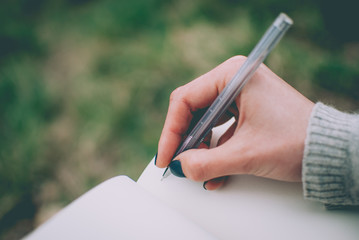 Blurred defocused background. Tender girl's pale hand writing in notebook with blank pages. Concept (idea) of dreaming, planning, motivation, studying.