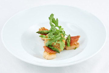 Delicious meal. Tasty dish with pieces of grilled fish, rusks, green leaves of arugula and asparagus on a white plate.