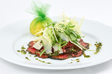 Delicious meal. Tasty fresh carpaccio of meat with few kinds of cheese, green leaves of arugula and lemon. 