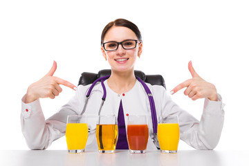Female nutritionist sitting in her working place showing and offering glass of pineapple orange apple tomato fresh juice on white background