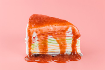 Homemade rainbow crape cake with red  strawberry sauce on pastel pink background.