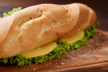 Fresh and tasty sandwich with cheese and vegetables on cutting board over wooden background, selective focus.
