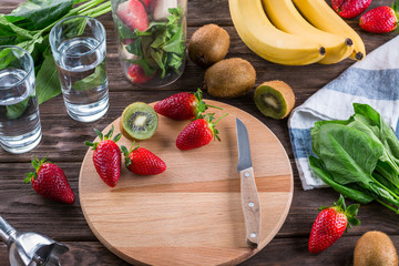 Preparing smoothies from spinach, banana, kiwi and strawberries on a wooden background