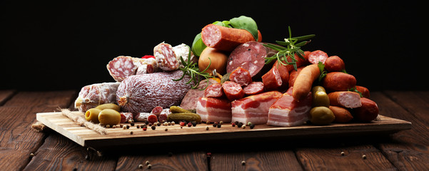 Food tray with delicious salami, ham,  fresh sausages, cucumber and herbs. Meat platter with...