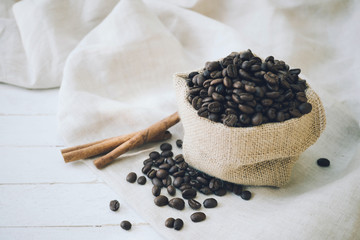 Fototapeta na wymiar Coffee beans in burlap sack and cinnamon on wood background
