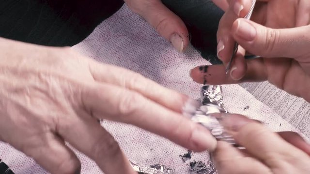 Manicurist removes the gel varnish from the nail of an elderly woman