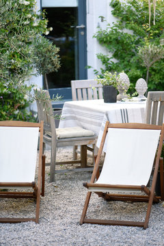 White loungers and table covered with white, gray and beige linen on a gravel terrace for a relaxing summer break