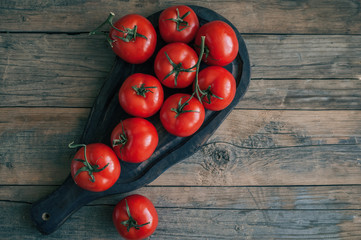 A large branch of ripe red tomatoes on a wooden figured blackboard in a rustic style.