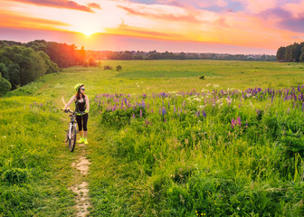 Young sporty woman riding a bicycle at sunset. Sporty girl goes uphill with bike and enjoy the...