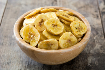 Banana chips in bowl on wooden table. 