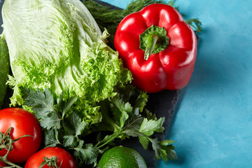 Refreshing close-up still life of assorted fresh vegetables and herbs on blue background, top view, selective focus.