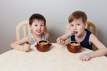 two little boys sit at the table and eat roast chicken and potatoes