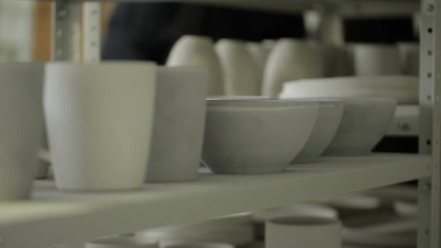 Close-up on the shelf is a white dish made of clay for drying. Cups and bowls are made in shape and stand colorless in anticipation of further processing of roasting and staining.