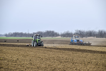 Obraz premium Lush and loosen the soil on the field before sowing. The tractor plows a field with a plow