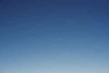 Imagen minimalista de cielo azul despejado con dos paracaidistas cayendo a lo lejos
